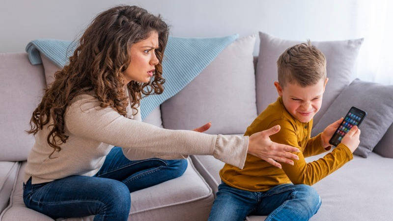 Adicción a la tecnología. Una madre intenta quitarle un smartphone de su hijo enfadado.
